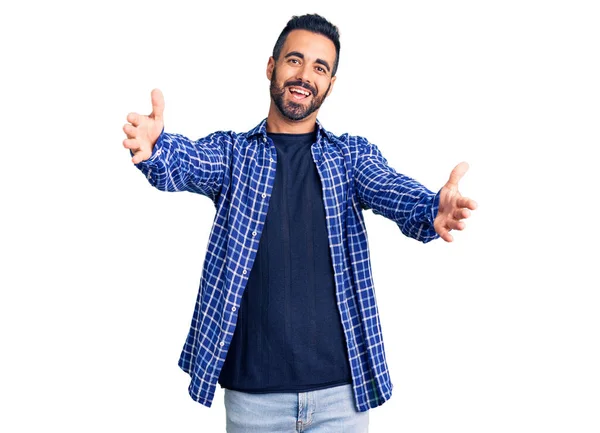 カジュアルな服を着た若いヒスパニック系の男が抱擁のために腕を開いて笑顔カメラを見ている 幸せを受け入れる陽気な表情 — ストック写真