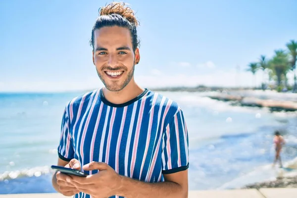 Ung Latinamerikansk Man Ler Glad Med Smartphone Stranden — Stockfoto