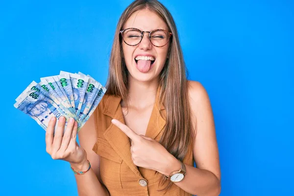 Güney Afrika rand banknotlarını tutan genç sarışın kız komik bir ifadeyle dilini dışarı çıkarıyor.. 