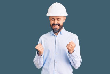 Mimar şapkalı yakışıklı genç adam başarı için heyecanlı kolları havada ve gözleri kapalı zaferi kutlarken gülümsüyor. Kazanan konsept. 