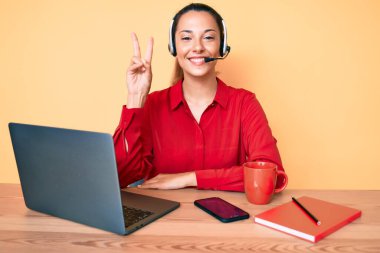 Çağrı merkezinde operatör kulaklığı takan genç esmer kadın kameraya gülümseyip zafer işareti yapıyor. İki numara.. 