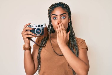 Saçları örgü örmüş, ağzı elle kapatılmış, şok olmuş ve hata yapmaktan korkan Afro-Amerikan bir kadın. şaşırmış ifade 