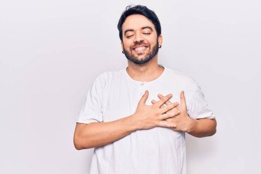 Gündelik kıyafetler giyen genç İspanyol adam elleri göğsünde, gözleri kapalı ve yüzünde minnet dolu bir jest ile gülümsüyor. sağlık kavramı. 