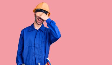 Genç İspanyol adam işçi üniforması giyiyor. Gülümsüyor ve gülümsüyor. Gözleri şaşkınlıkla örtüyor. kör kavram. 