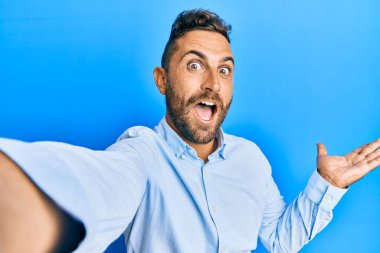 Sakallı yakışıklı bir adam akıllı telefonuyla fotoğraf çekiyor zaferi kutluyor mutlu bir gülümseme ve ellerini kaldırarak kazanan yüz ifadesi. 