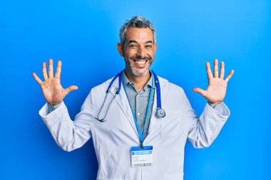 Orta yaşlı, gri saçlı, doktor üniforması giyen ve steteskop kullanan bir adam on numarayı gösterip işaret ederken kendinden emin ve mutlu bir şekilde gülümsüyor.. 