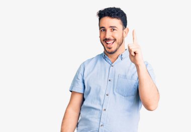 Gündelik kıyafetler giyen genç İspanyol adam başarılı bir fikirle işaret ediyor. Heyecanlı ve mutlu. Bir numara.. 