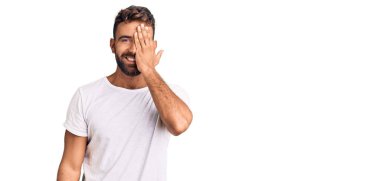 Latin kökenli genç bir adam, günlük beyaz tişört giyiyor. Bir gözünü eliyle kapatıyor. Yüzünde kendine güvenen bir gülümseme ve sürpriz bir duygu var.. 