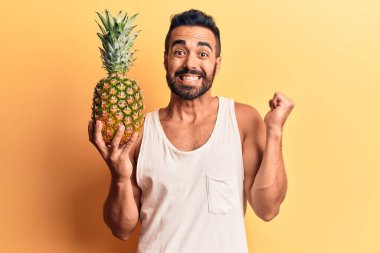 Genç İspanyol adam ananas tutuyor gururla bağırıyor, zaferi kutluyor ve başarıyı kollarını kaldırarak kutluyor. 
