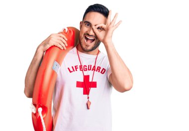 Cankurtaran üniforması giymiş genç yakışıklı elinde şamandıra, gülümsüyor. 