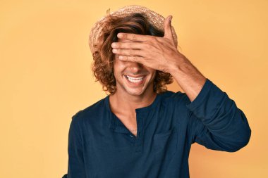 Yaz şapkası takan, gülümseyen ve gülen genç İspanyol adam şaşırmak için gözlerini kapatıyor. kör kavram. 