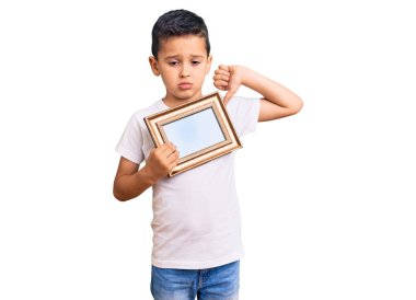 Küçük sevimli çocuk elinde boş bir çerçeve tutuyor, kızgın yüzlü, negatif işaret baş parmakları aşağıda, reddedilme konsepti. 