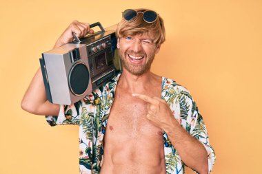 Yaz tarzı giyinmiş genç bir adam elinde teyp ile kameraya bakıyor. Seksi bir ifadeyle, neşeli ve mutlu bir yüzle.. 