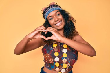 Genç Afro-Amerikan kadın bohem ve hippi tarzı giyiniyor. Sevgiyle gülümsüyor. Kalp sembolü ve elleri ile şekil veriyor. romantik kavram. 