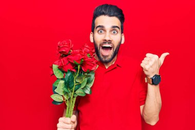 Genç, sakallı, elinde gül buketi olan yakışıklı bir adam baş parmağını yana kaldırmış, ağzı açık gülümsüyor. 