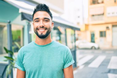 Genç Arap adam gülümsüyor, şehirde mutlu bir şekilde yürüyor..