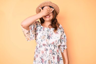 Yazlık elbise giyen, şapkalı, gülümseyen ve gülen genç, güzel, beyaz bir kadın şaşkınlık için gözlerini kapatıyor. kör kavram. 