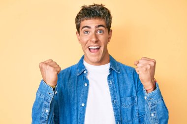 Gündelik giysiler giyen genç yakışıklı adam şaşkınlık ve şaşkınlık içinde kollarını kaldırarak ve gözlerini açarak başarıyı kutluyor. Kazanan konsept. 