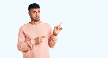 Gündelik kıyafetler giyen genç İspanyol bir adam iki eliyle endişeli ve endişeli bir ifadeye işaret ediyor. 