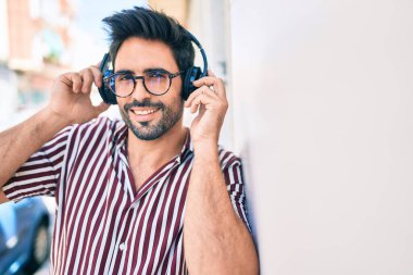 Sakallı, neşeli, kulaklık takmış, müzik dinleyen yakışıklı İspanyol bir adam.