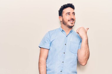 Gündelik giysiler giymiş genç İspanyol bir adam baş parmağını yana kaldırıyor ve ağzı açık gülümsüyor. 