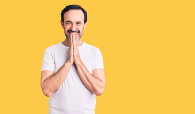 Orta yaşlı yakışıklı bir adam sıradan bir tişört giyip ellerinin birarada dua ederek af diliyor kendinden emin bir şekilde gülümseyerek.. 