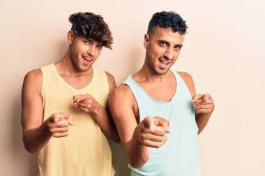 Gündelik giysiler giyen genç eşcinsel çift mutlu ve komik yüzlü parmaklarını kameraya doğrultuyor. iyi enerji ve titreşimler. 