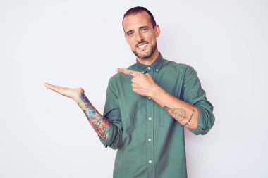 Dövmeli genç ve yakışıklı bir adam gündelik giysiler giyiyor. Kameraya hayret ediyor ve gülümsüyor. Elle ve parmakla işaret ediyor.. 