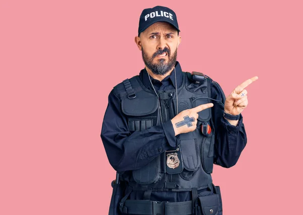 Young handsome man wearing police uniform pointing aside worried and nervous with both hands, concerned and surprised expression