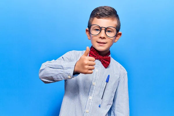 かわいいブロンドの子供はオタクの弓ネクタイと眼鏡をかけて手で幸せな親指を上げてジェスチャーをします 成功を示すカメラを見ると — ストック写真