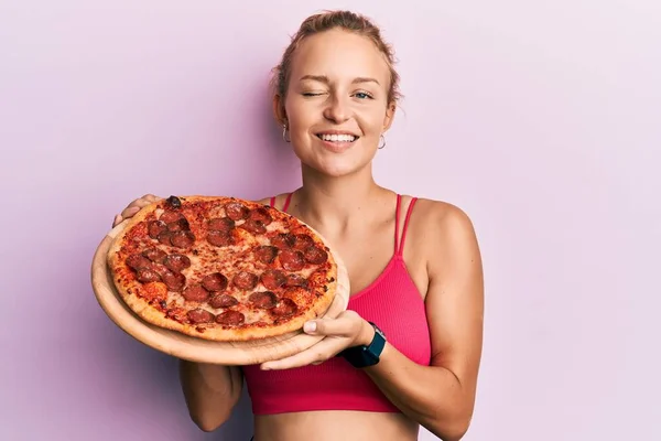 拿着意大利披萨的美丽的高加索女人眨了眨眼 带着性感的表情 笑容满面地看着摄像机 — 图库照片
