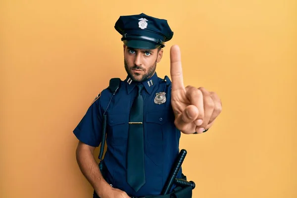 Handsome hispanic man wearing police uniform pointing with finger up and angry expression, showing no gesture