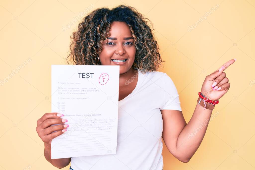 Young african american plus size woman showing a failed exam smiling happy pointing with hand and finger to the side 