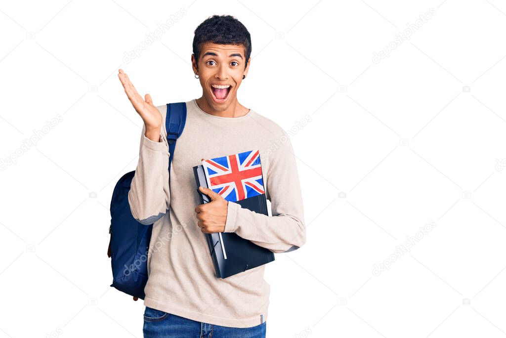 Young african amercian man wearing student backpack holding binder and uk flag celebrating victory with happy smile and winner expression with raised hands 