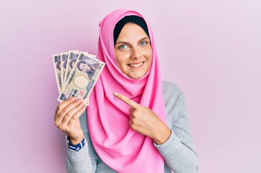 Kafkasyalı genç bir kadın, elinde Japon Yen banknotları tutarak el ve parmağıyla mutlu bir şekilde işaret ediyor. 