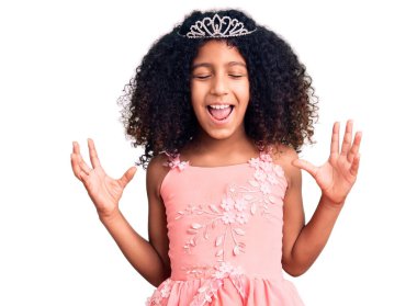 African american child with curly hair wearing princess crown celebrating mad and crazy for success with arms raised and closed eyes screaming excited. winner concept  clipart