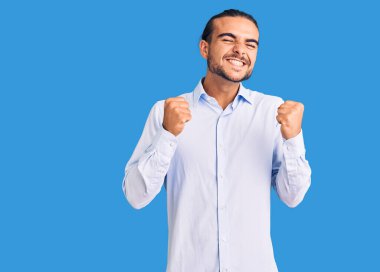 İş elbiseleri giyen genç yakışıklı adam başarı için heyecanlanıyor kolları havada ve gözleri kapalı zaferi kutluyor gülümsüyor. Kazanan konsept. 