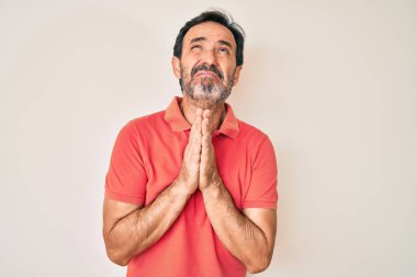 Orta yaşlı İspanyol bir adam gündelik giysiler giyip elleri bağlı yalvarıyor ve dua ediyor. Yüzünde umut ifadesi var. Çok duygusal ve endişeli. Yalvarıyor. 