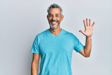 Orta yaşlı, gri saçlı, günlük kıyafetler giyen, beş numaralı parmaklarıyla işaret eden, kendinden emin ve mutlu bir adam.. 