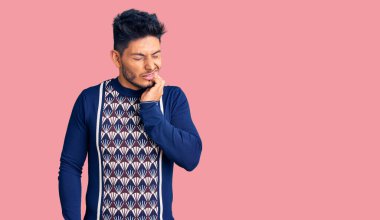 Yakışıklı Latin Amerikalı sıradan bir kazak giymiş diş ağrısı ya da diş hastalığından dolayı acı dolu bir ifadeyle ağıza dokunuyor. dişçi 