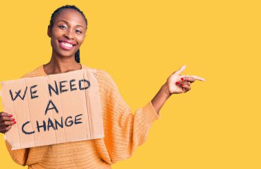 Genç Afrikalı Amerikalı kadın elinde bir değişiklik pankartı tutarken mutlu bir gülümsemeye ihtiyacımız var. 