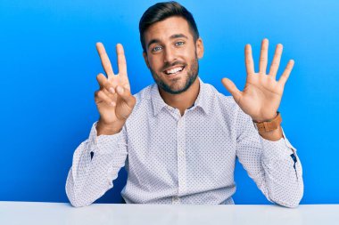 Yakışıklı, iş kıyafetleri giyen, masada oturan, 7 numaralı parmaklarıyla işaret eden, kendine güvenen ve mutlu bir İspanyol.. 