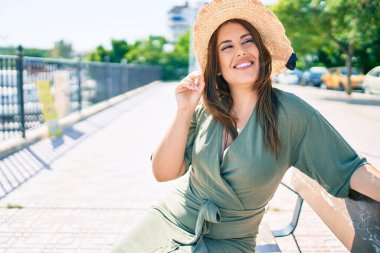 Genç İspanyol kadın tatilde gülümsüyor. Mutlu bir şekilde şehrin sokaklarında bankta oturuyor.