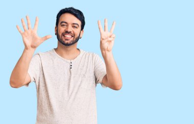 Gündelik kıyafetler giyen genç İspanyol adam sekiz numarayı gösterip işaret ederken kendinden emin ve mutlu bir şekilde gülümsüyor.. 