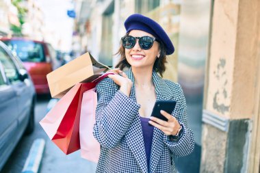Fransız tarzı güzel bir kız alışveriş torbaları tutuyor. Şehir caddesinde akıllı telefon kullanıyor.