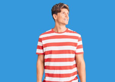 Gündelik giysiler giymiş genç yakışıklı bir adam yüzünde gülümsemeyle yan yana bakıyor, doğal bir ifade. Kendinden emin gülen. 