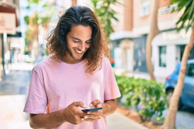 Genç İspanyol adam şehirde akıllı telefon kullanarak mutlu gülümsüyor..