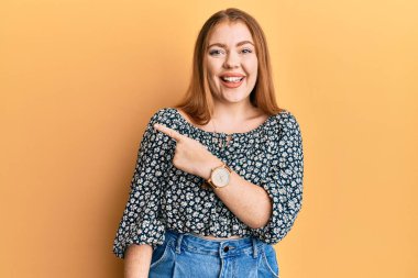 Çiçek desenli tişört giyen güzel, kızıl saçlı bir kadın. Gülümsüyor, eli ve parmağı yana doğru uzanıyor. 