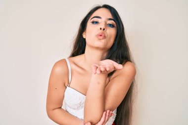 Esmer, zarif pozlar veren genç bir kız kameraya bakıp havada bir öpücük savuruyor ve sevimli ve seksi oluyor. aşk ifadesi. 