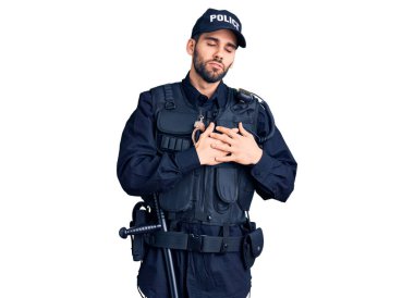 Sakallı, polis üniforması giyen, elleri göğsünde, gözleri kapalı gülümseyen ve yüzünde minnet ifadesi olan genç yakışıklı bir adam. sağlık kavramı. 
